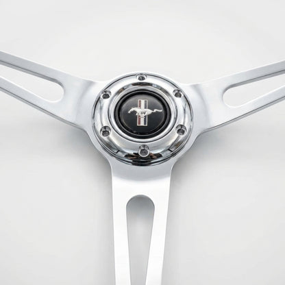 A close-up of a polished chrome steering wheel rim with a black center cap featuring the silver Mustang horse logo.