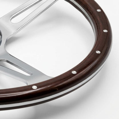 Close-up of a steering wheel rim with a dark brown wood inlay and polished silver metal spokes, secured by silver rivets, on a white background.
