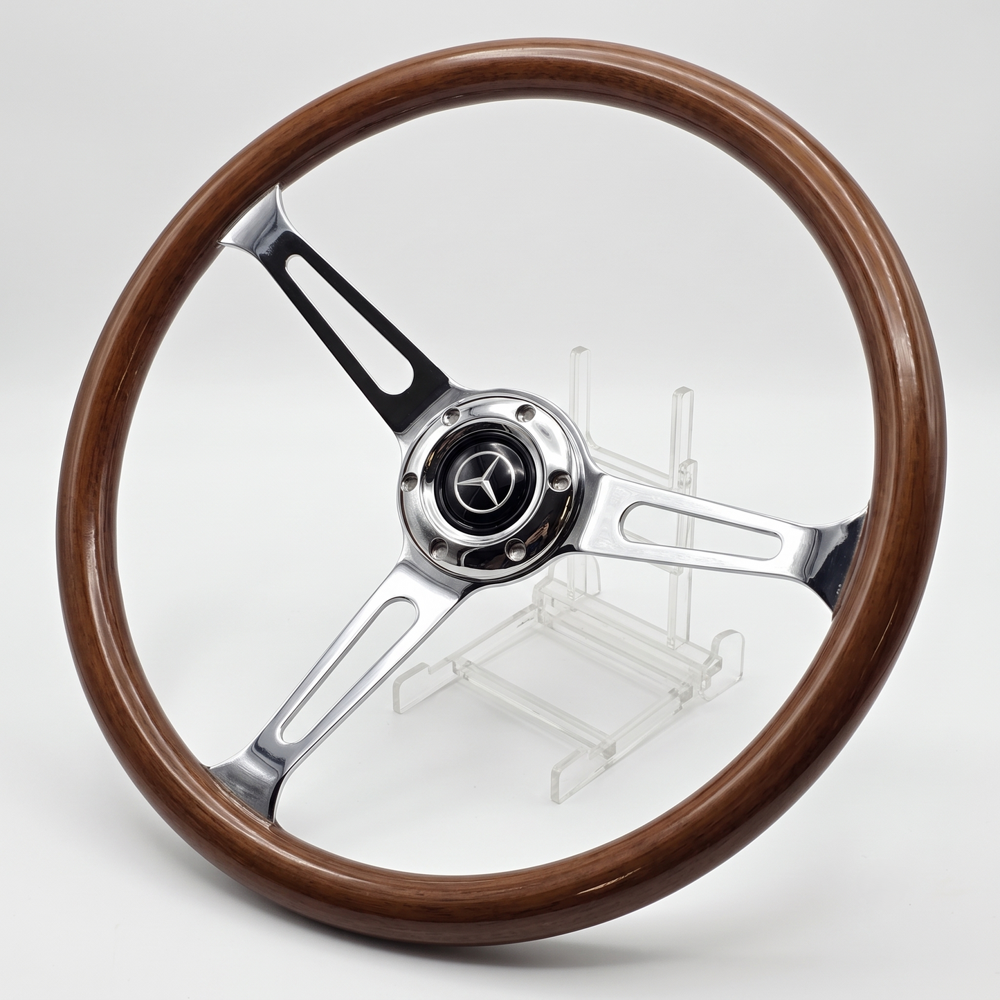 A classic three-spoke car steering wheel with a polished brown wood rim and polished silver metal spokes, featuring a Mercedes-Benz star emblem in the center, displayed on a clear stand against a light gray background.