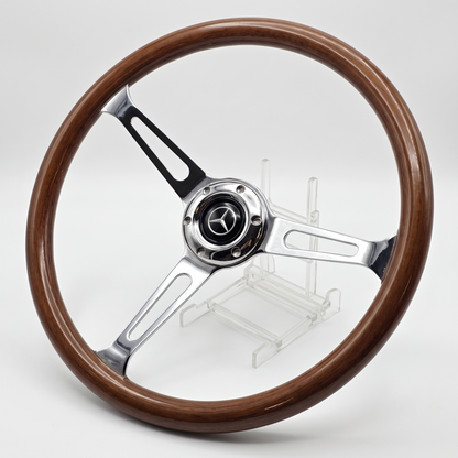 A classic three-spoke car steering wheel with a polished brown wood rim and polished silver metal spokes, featuring a Mercedes-Benz star emblem in the center, displayed on a clear stand against a light gray background.