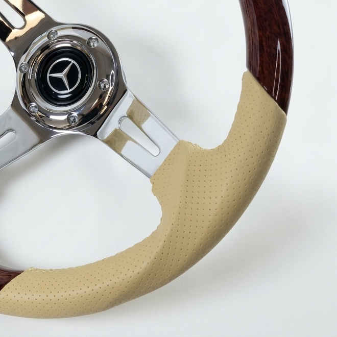 A close-up of a steering wheel featuring a beige perforated leather grip wrap, dark brown wood spokes, and a polished chrome center hub with a Mercedes-Benz star logo.