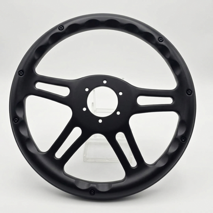 A matte black multi-spoke steering wheel rim with a central hub and decorative outer lip, photographed on a clean light gray studio background.