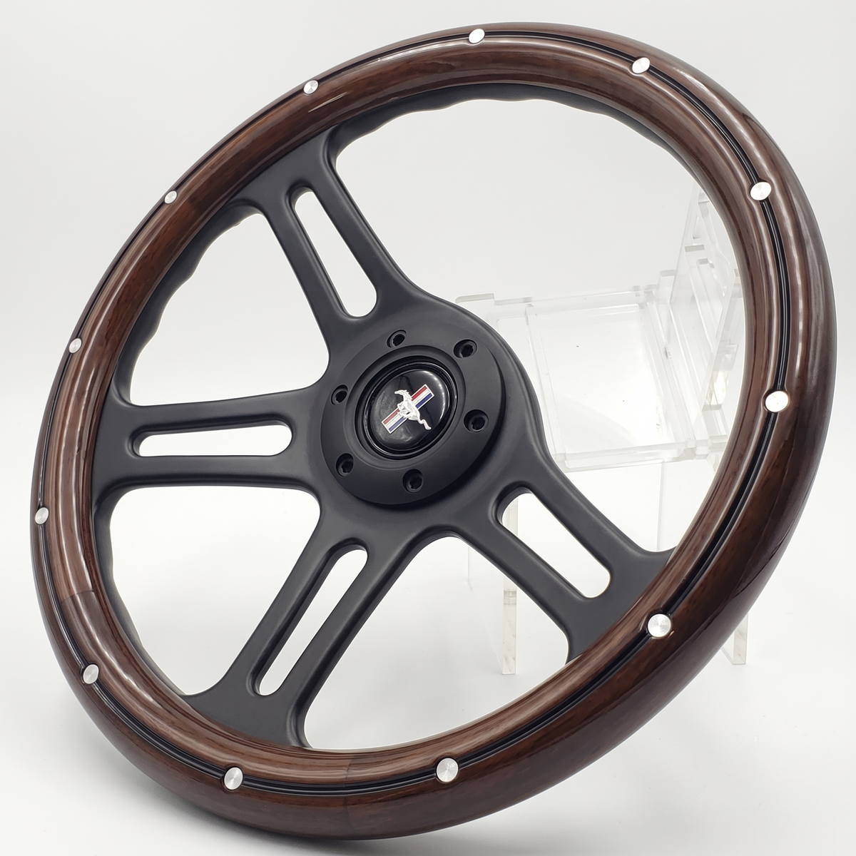 A custom car steering wheel featuring a glossy black five-spoke center and a dark brown wood-grain outer rim accented with silver rivets, displayed on a clear acrylic stand against a white studio background.