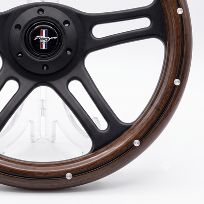 Close-up of a custom steering wheel featuring a dark brown wood grain rim, a matte black multi-spoke center, and a black horn button with a Mustang logo.