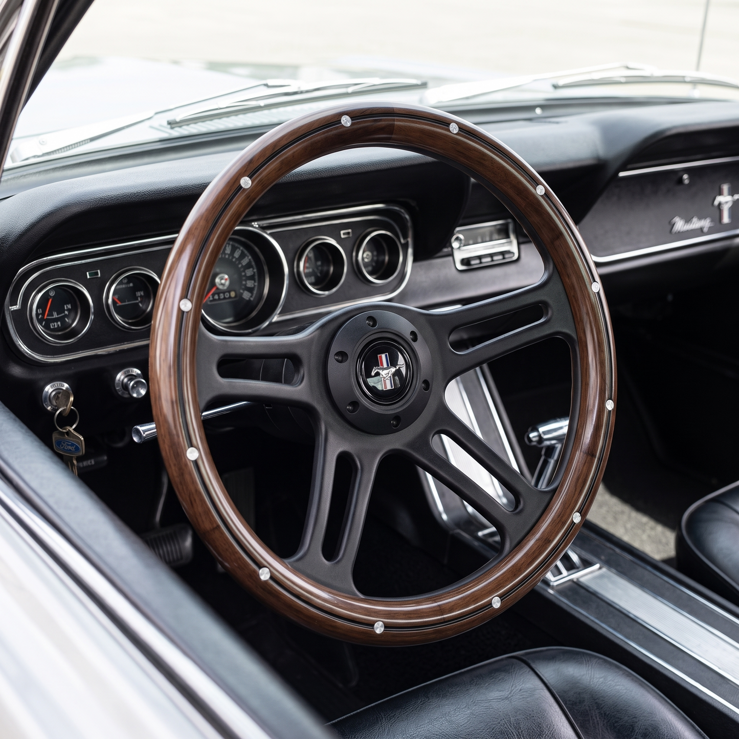 A close-up of a vintage-style car interior featuring a wood-rimmed black steering wheel with silver rivets, a black dashboard, and a Mustang emblem in the center.