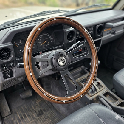 A custom wooden steering wheel with a black center and silver rivets, installed in a vintage Toyota truck cabin.