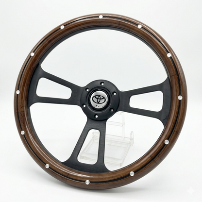 A custom car steering wheel featuring a dark brown wood grain outer rim with silver rivets, a matte black three-spoke center, and a central Toyota emblem.